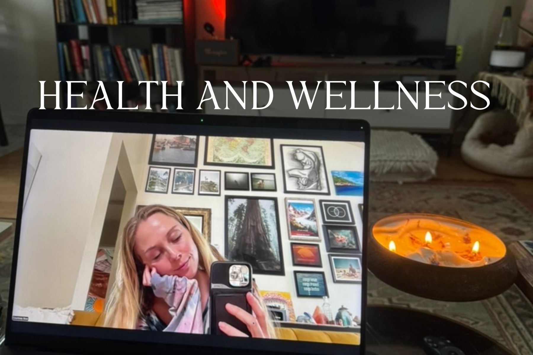 A laptop displaying a woman taking a selfie in a room with a wall decorated with framed pictures and artwork, a lit candle holder shape of a boat with three candles, and a bookshelf in the background. The words 'Health and Wellness' are overlaid on the image.
