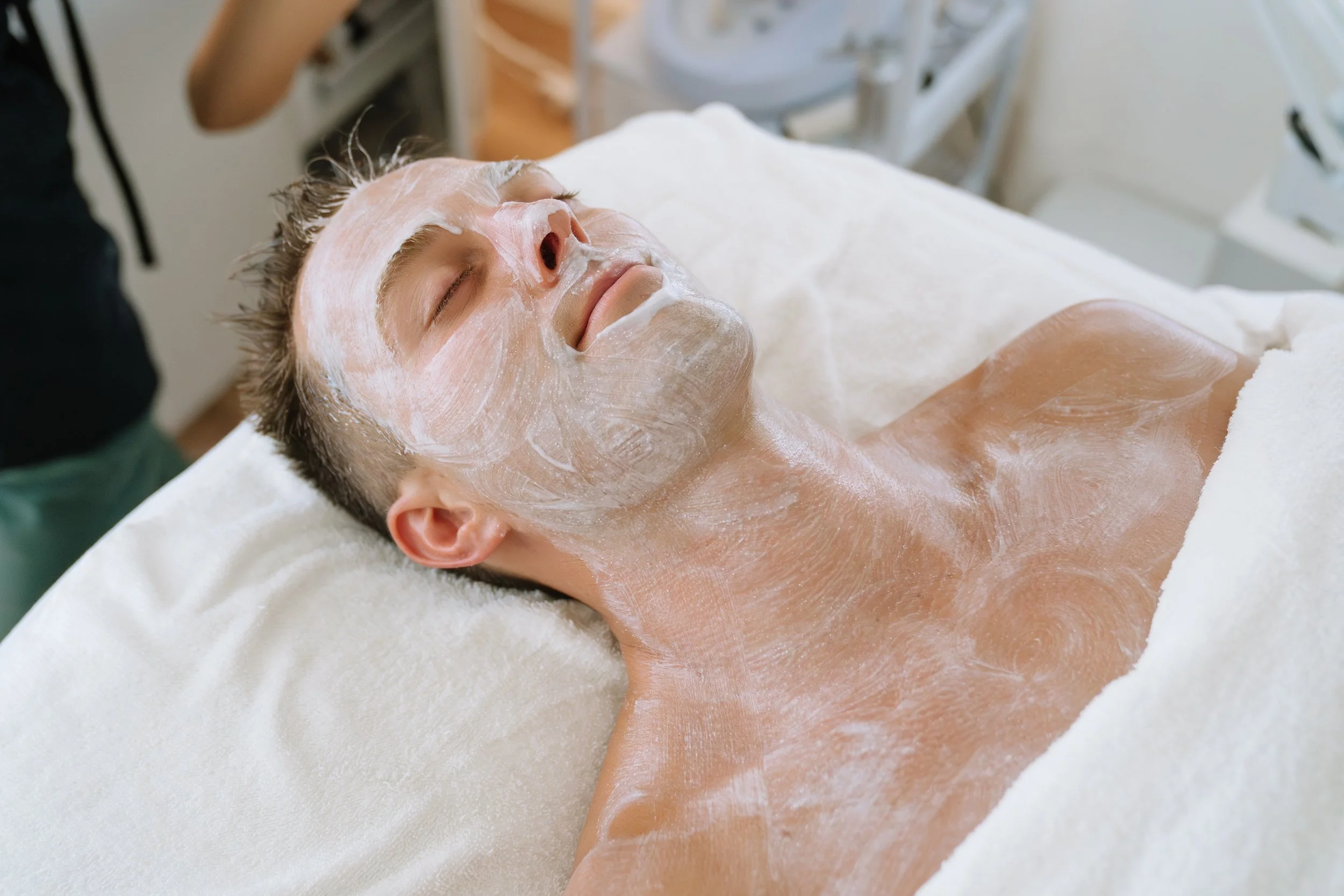 A person lying on a spa bed with a facial mask applied, eyes closed, and relaxed.