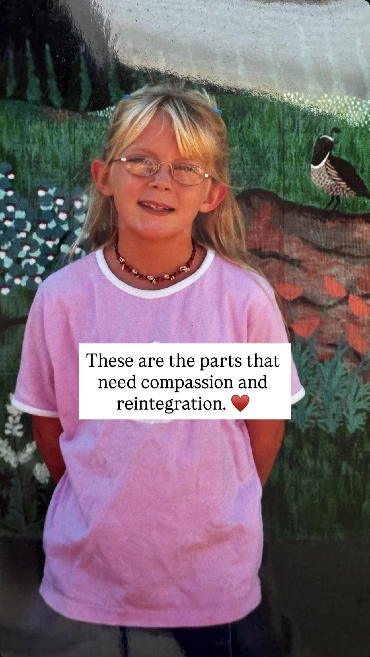 A young girl with glasses and blonde hair, smiling, wearing a pink shirt and a beaded necklace, standing in front of a mural with nature and bird illustrations. An overlay text says, 'These are the parts that need compassion and reintegration.'