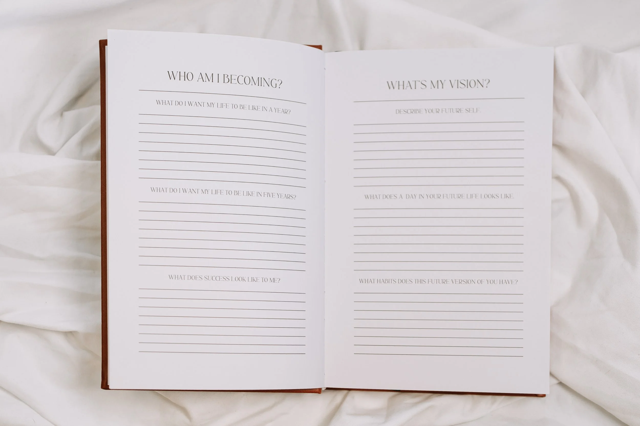 Open journal with writing prompts about personal growth and future goals, resting on white fabric.