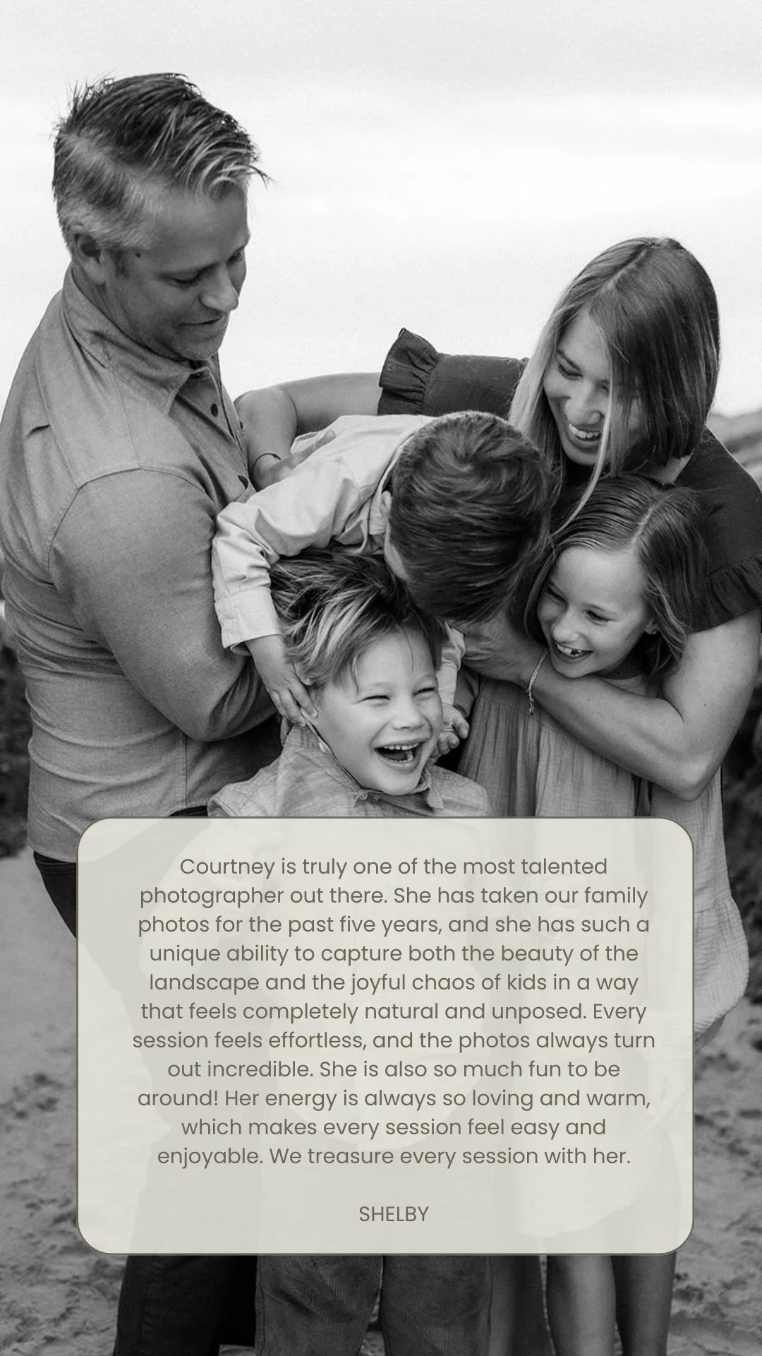 A black and white photo of a happy family of five, with two adults and three children, laughing and playing outdoors. The adults are embracing the children, who are smiling and laughing, in a joyful moment.