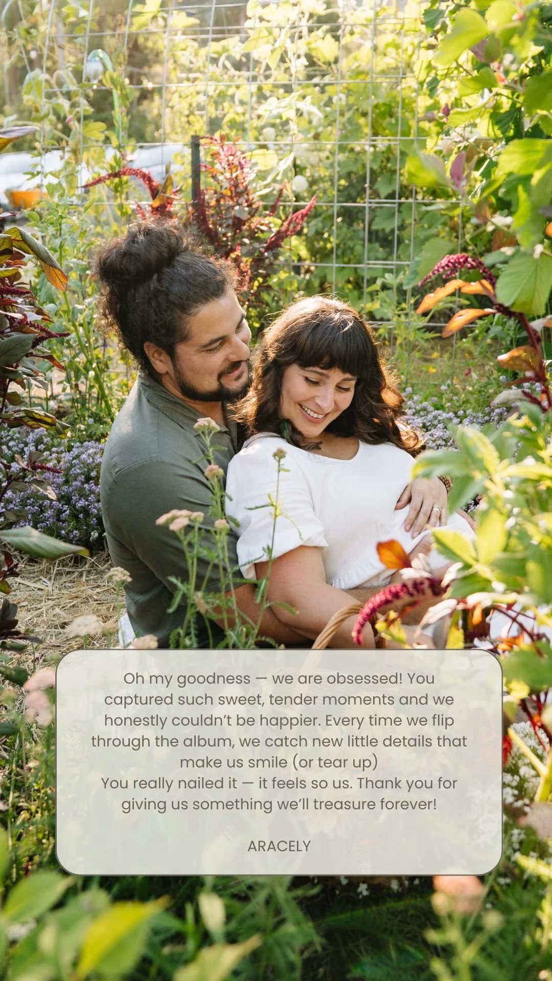 A couple smiling and embracing in a lush garden with green and purple plants, sunlight shining through the foliage.