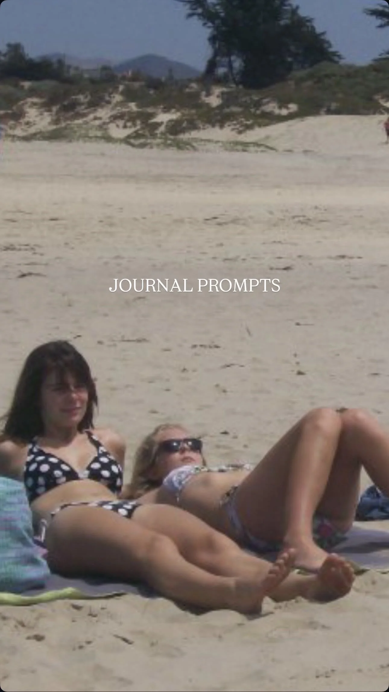 Two women in swimsuits lying on the sandy beach with the text 'JOURNAL PROMPTS' overlaid.