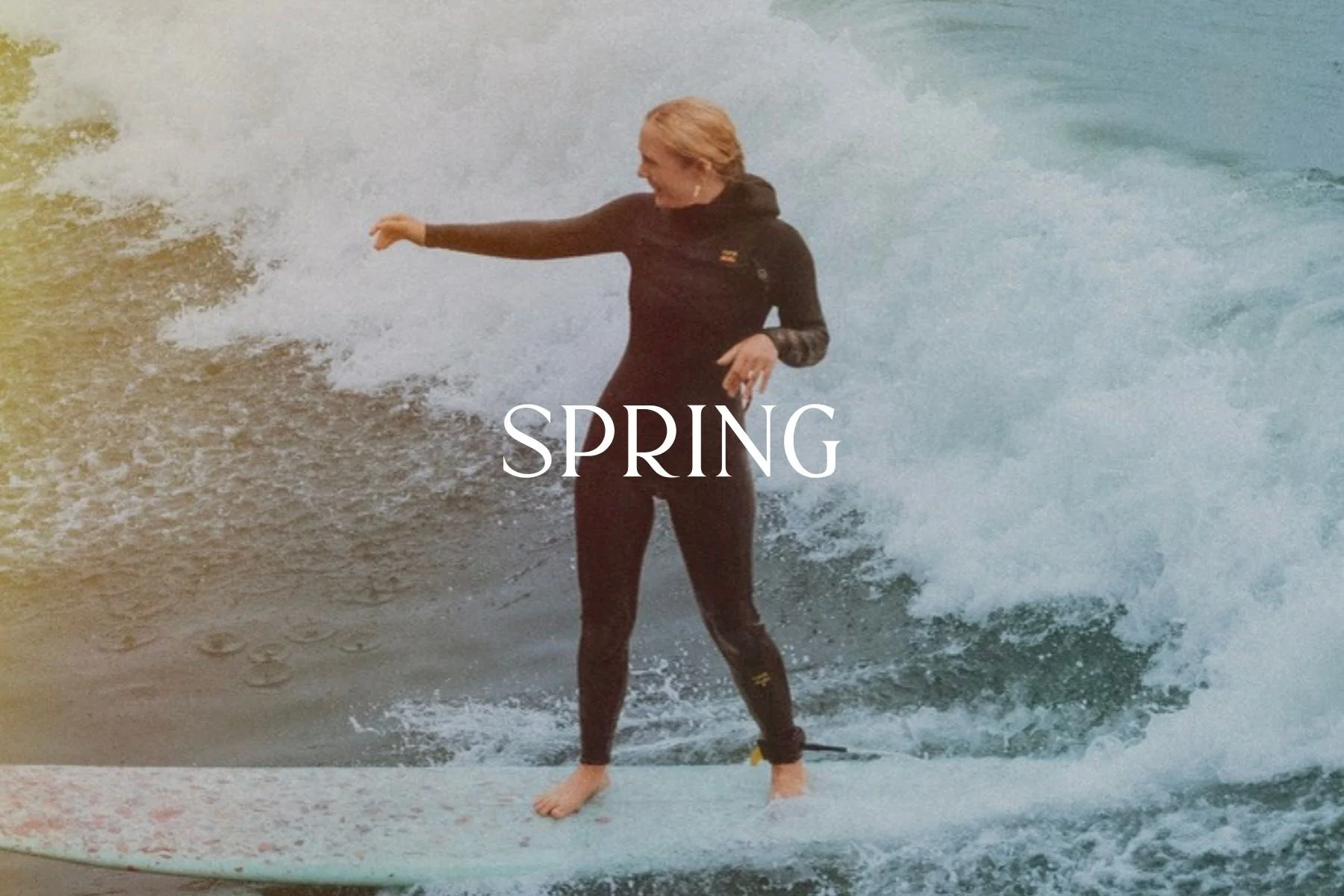 A woman in a wetsuit standing on a surfboard riding a wave in the ocean during spring.