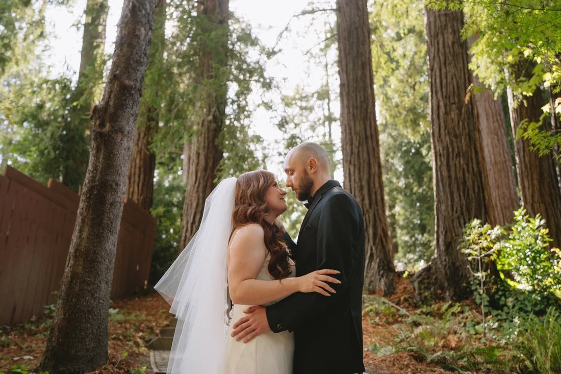 A bride and groom standing close in a forest, gazing into each other's eyes during their wedding.