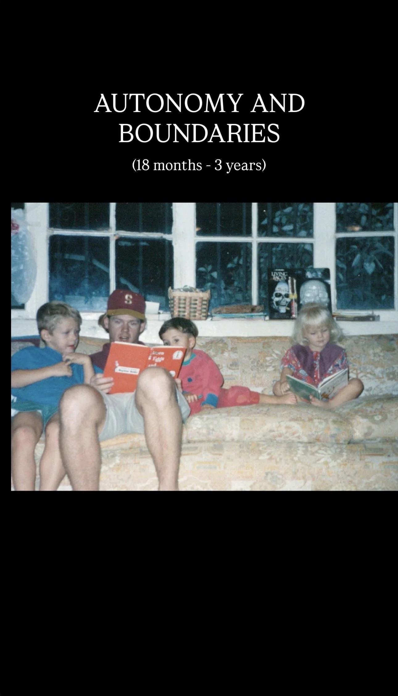 A family sitting on a floral-patterned couch reading books in a living room with large windows in the background.