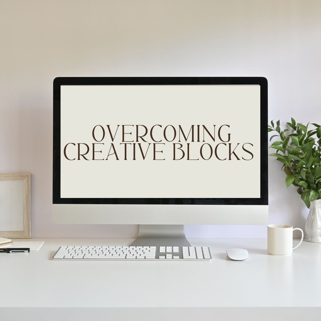 Computer screen displaying the words "Overcoming Creative Blocks" with a white desk, keyboard, mouse, a mug, a framed picture, and a green plant.