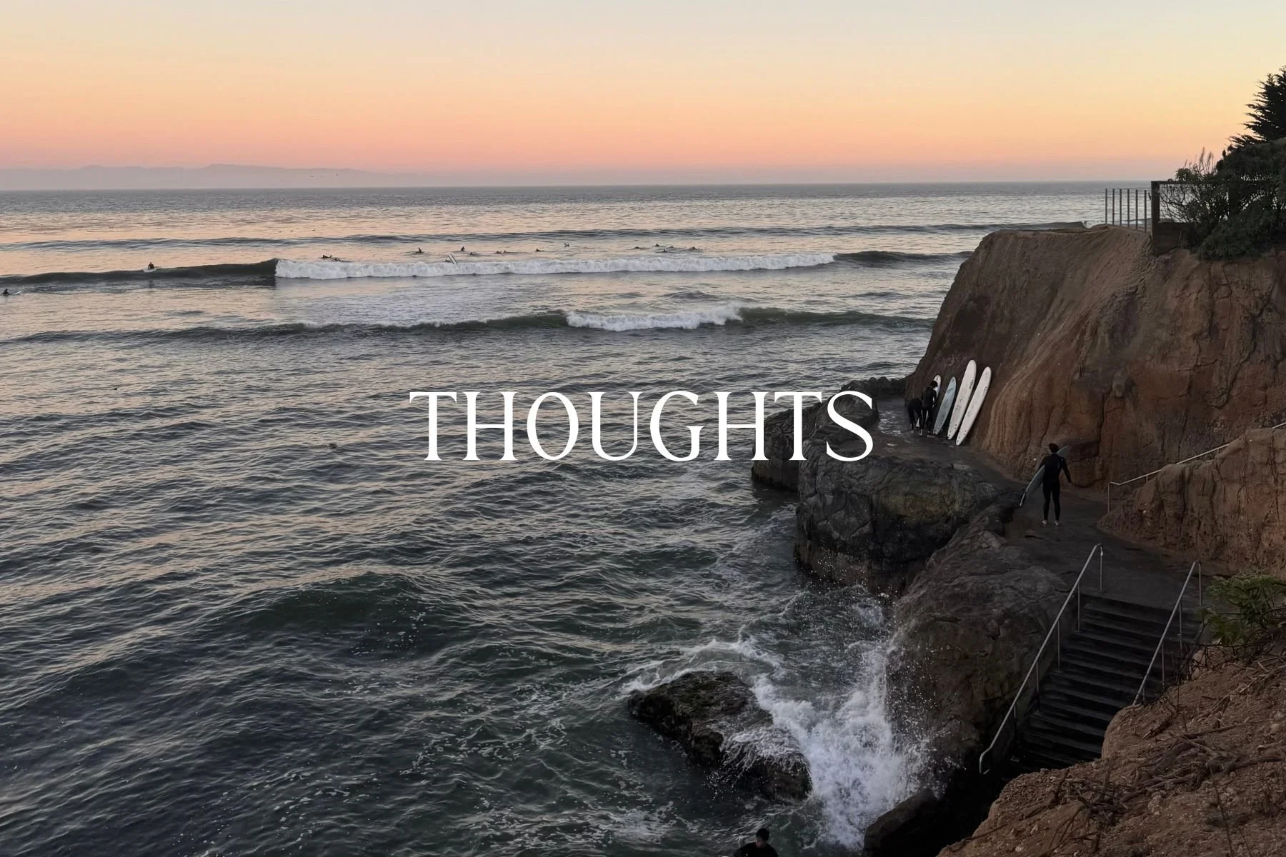 A sunset over the ocean with surfers riding waves and surfboards leaning against a rocky cliff. The word 'THOUGHTS' is written across the center of the image.