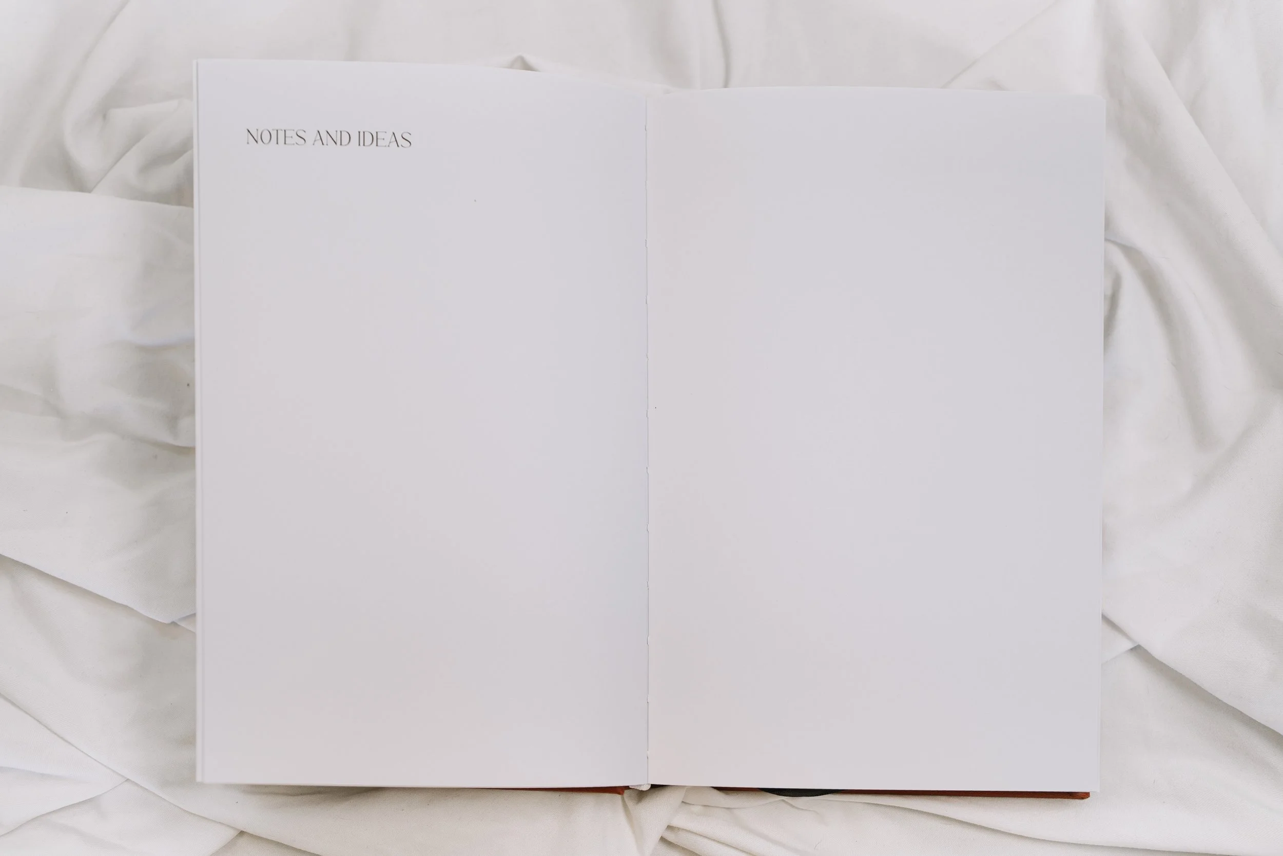 Open notebook with the title 'NOTES AND IDEAS' on the left page, resting on white fabric surface.