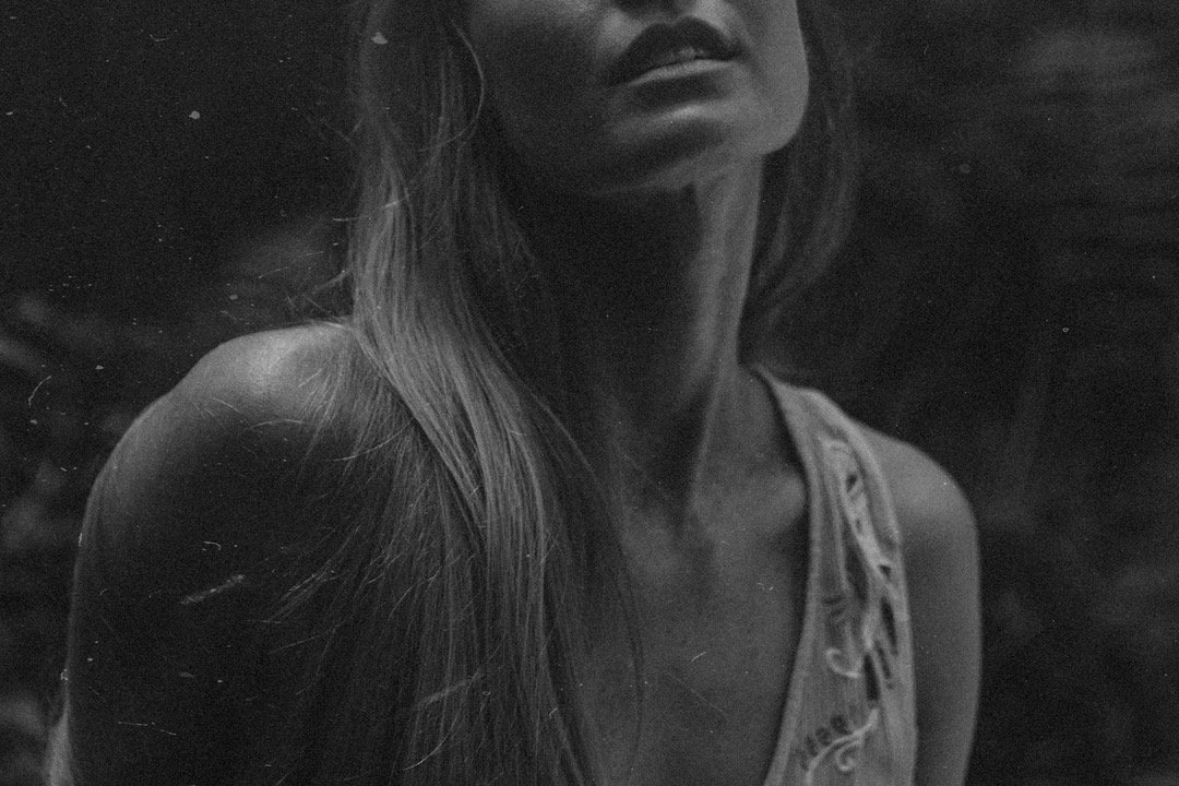 Black and white photograph of a woman with long hair and a sleeveless top, with part of her face and neck visible.