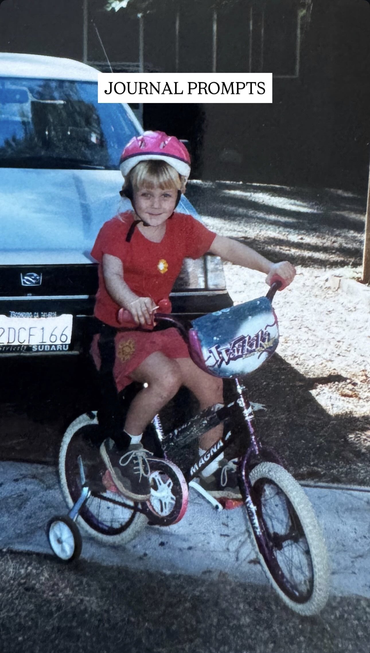 A young girl wearing a pink bike helmet and red shirt riding a bicycle with training wheels in front of a car with a Subaru license plate.