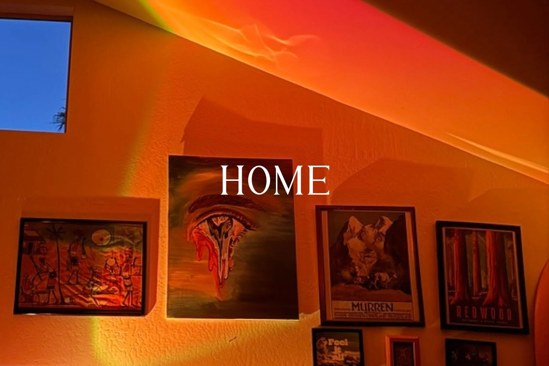 Decorated wall with framed artwork, including a colorful painting, a poster of a wolf labeled 'MURREN,' and a poster of a forest labeled 'REDFWOOD,' with warm orange lighting.