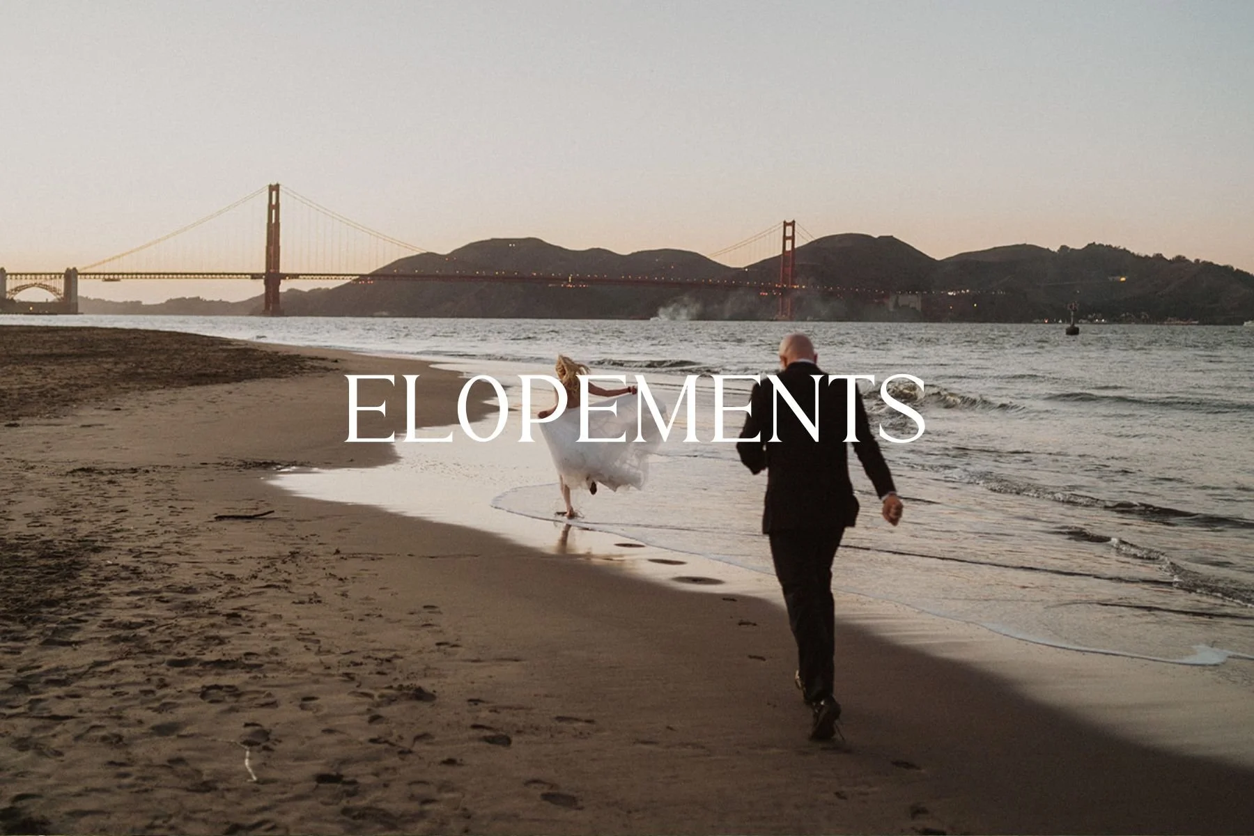 A bride and groom walk along the beach in wedding attire at sunset, with the Golden Gate Bridge in the background.
