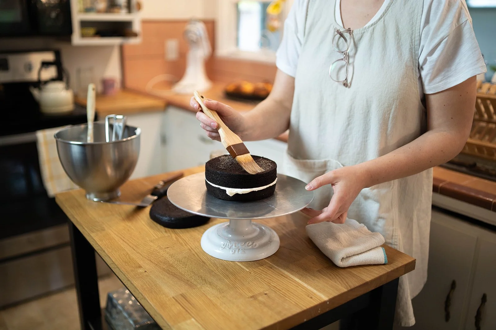 Person decorating a black chocolate cake with a spatula in a kitchen.