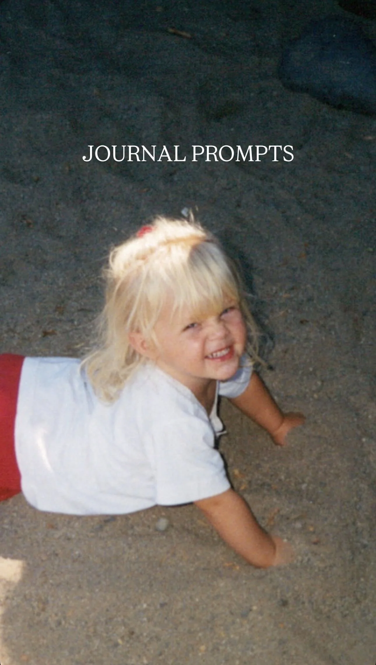 A young girl with blonde hair, smiling and crawling on the ground, wearing a white shirt and red shorts, with "JOURNAL PROMPTS" text overlayed.