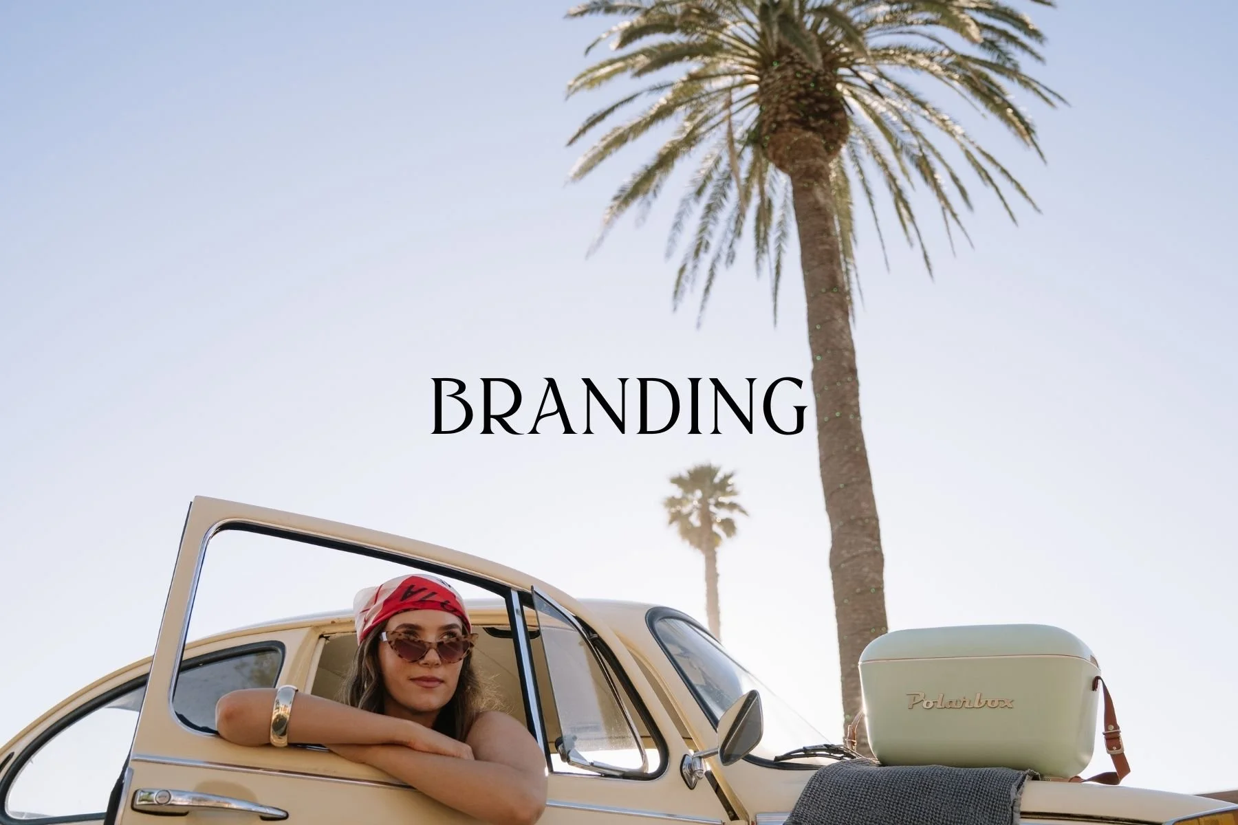 A woman with sunglasses and a pink hat leaning on a vintage yellow car in a beach setting with palm trees, with the word 'BRANDING' overlaid in the sky.