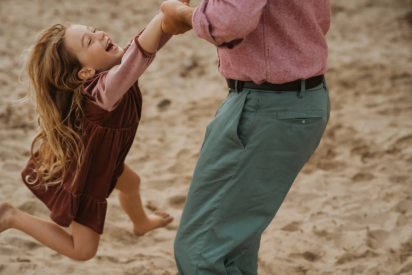 Little girl laughing with dad at the beach during family photoshoot