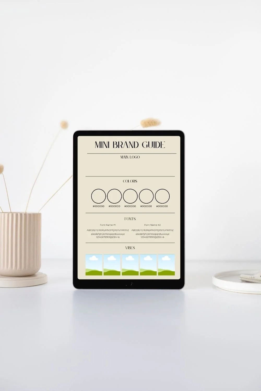 Digital mockup of a mini brand guide on a tablet, showing sections for logo, colors, fonts, and vibes, on a white desk with a beige vase with dried flowers on the left and a white tray on the right.