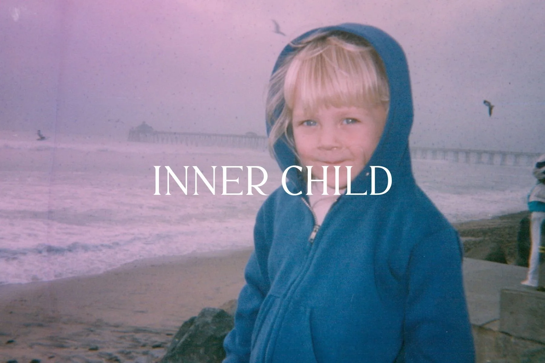 Young child with blond hair and blue eyes wearing a blue hoodie on a beach with waves and a pier in the background, with the text "INNER CHILD" overlaid.