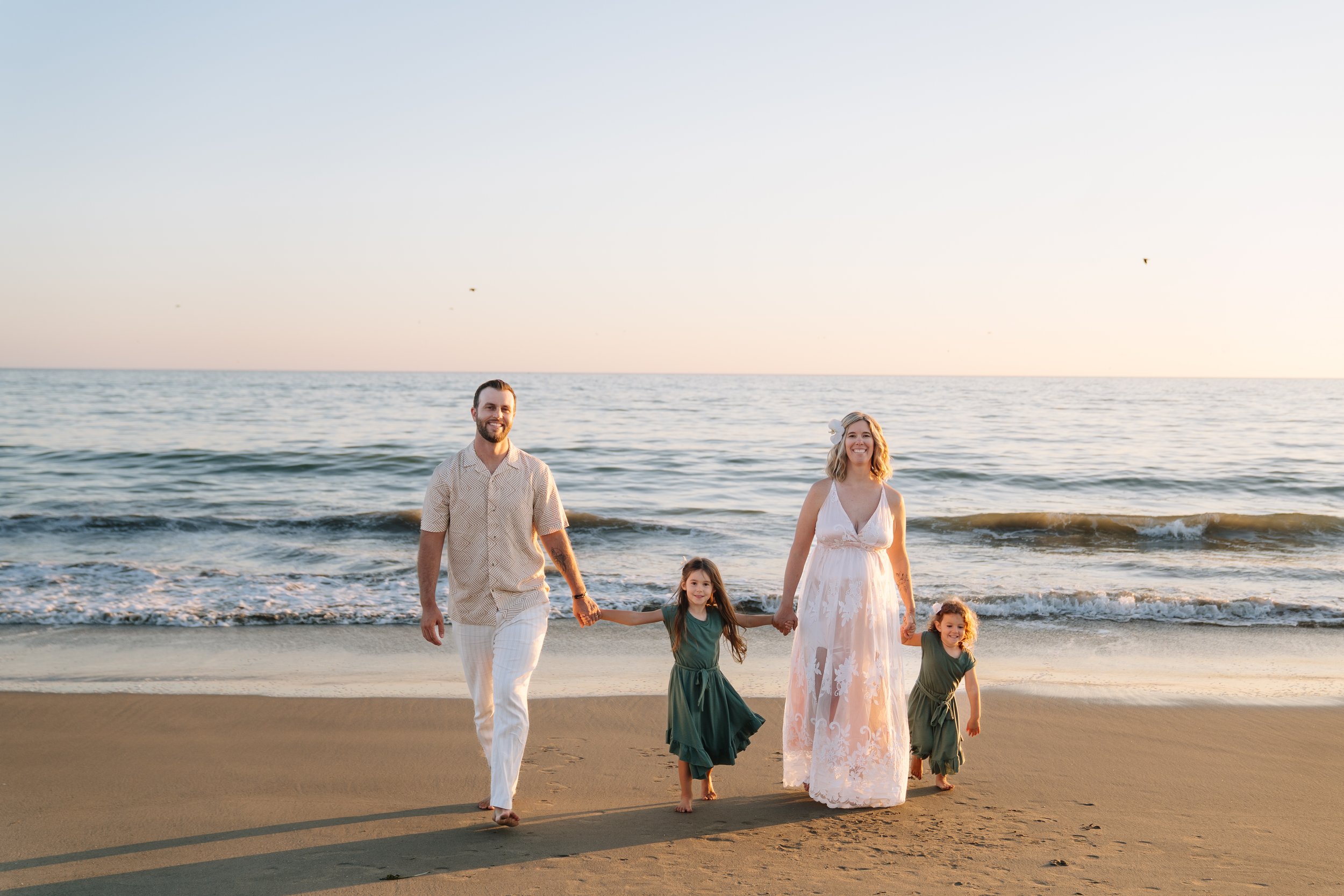 A family walking on the beach at sunset, holding hands, with the ocean in the background.