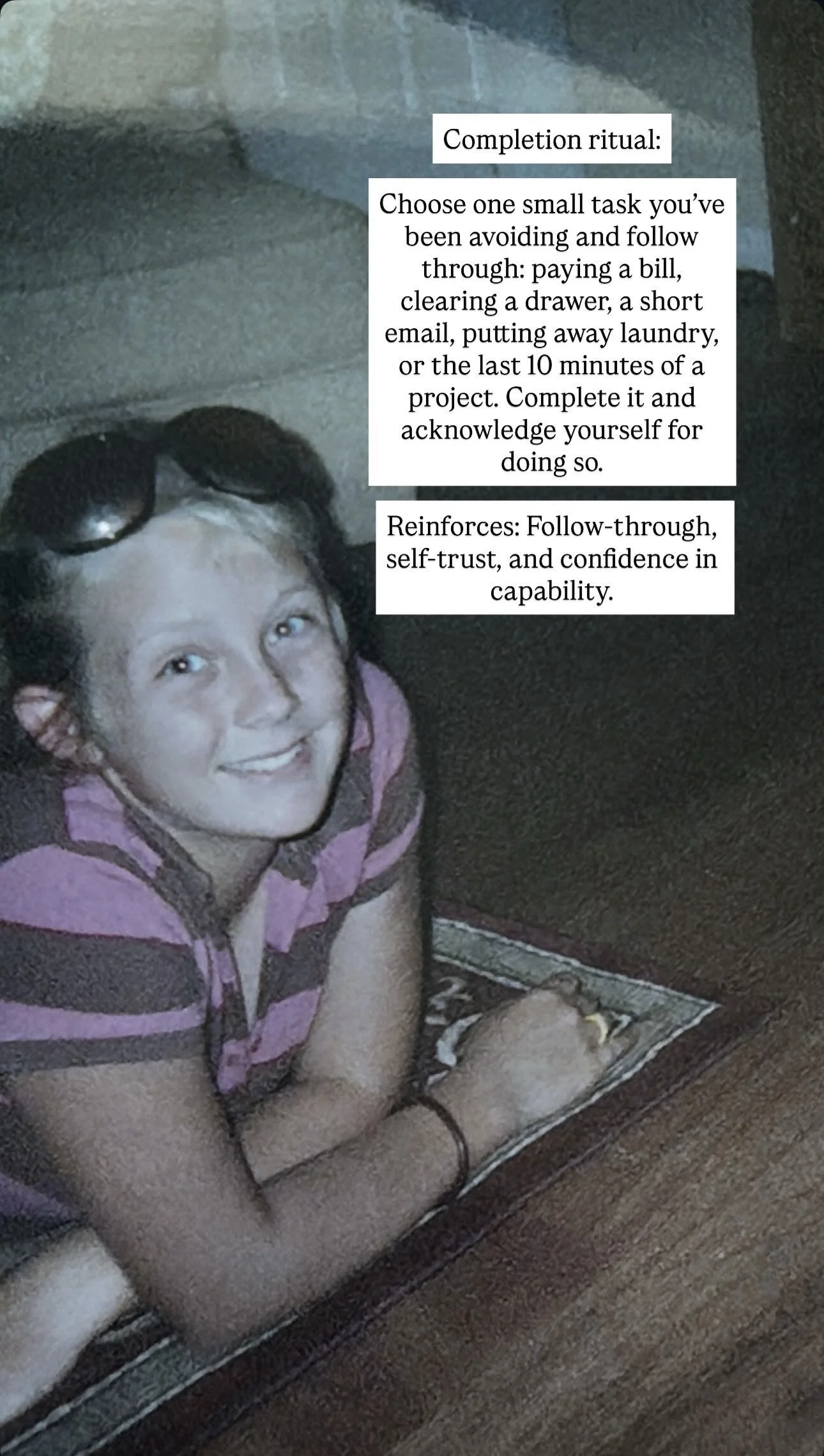 A smiling girl with glasses on her head, wearing a pink and brown striped shirt, lying on her stomach on a small rug on a wooden floor, with a white wall in the background. Overlaid text provides a completion ritual and reinforcement suggestions.