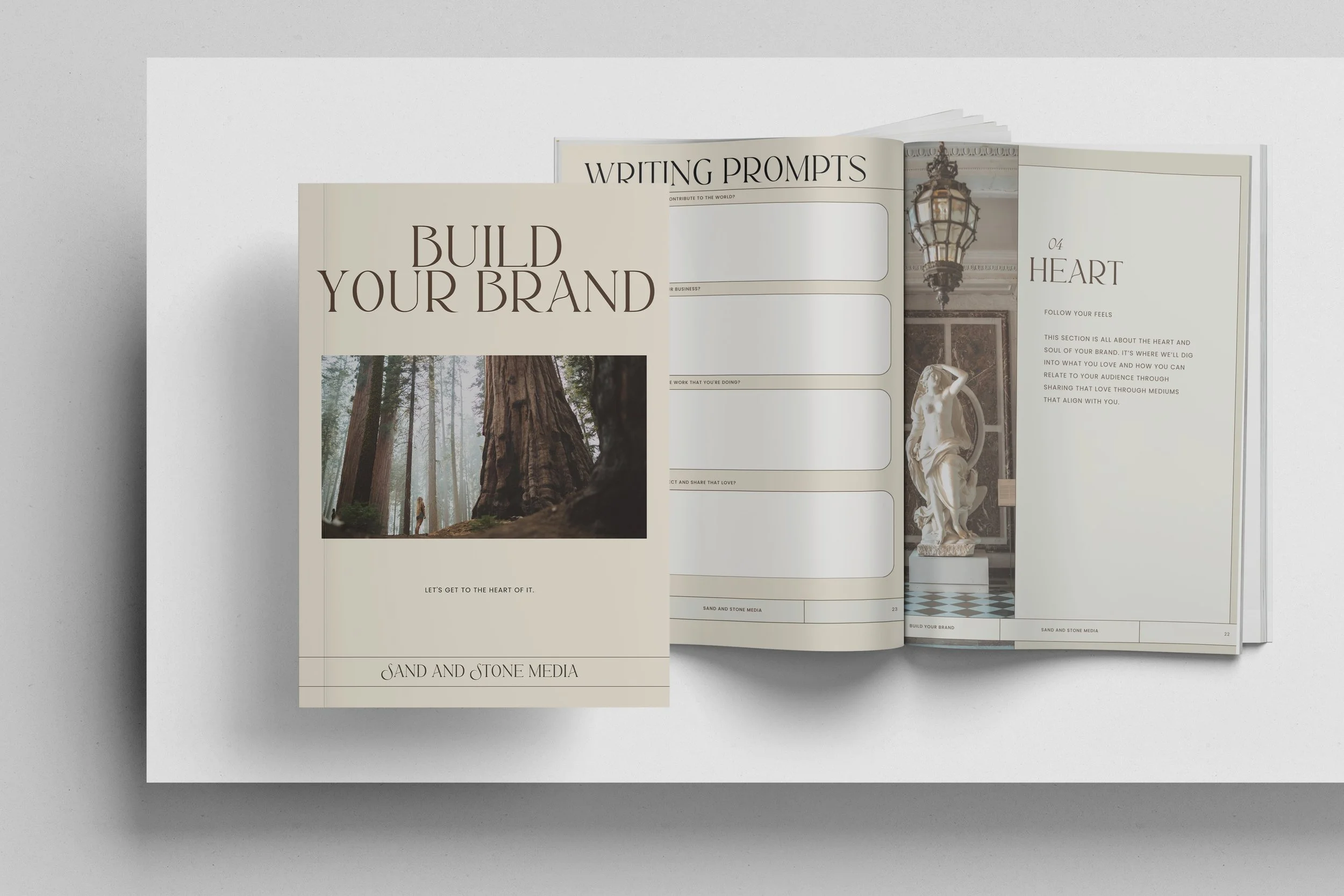 Open magazine with the cover page titled "Build Your Brand" featuring a forest scene with tall trees and a person walking. Inside the pages, there are writing prompts, an image of a chandelier, a statue, and a section titled "Heart" about connecting with your audience.