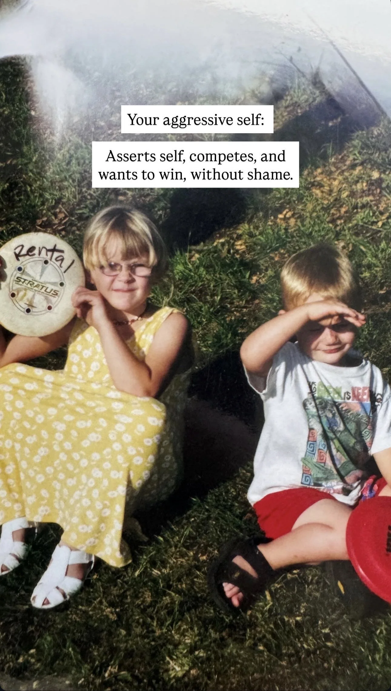 A young girl and a boy sitting outside on grass. The girl is holding a disc with the word 'Rental' written on it and is wearing a yellow dress. The boy is shielding his eyes from the sun with his hand and is wearing a gray T-shirt with a graphic and 