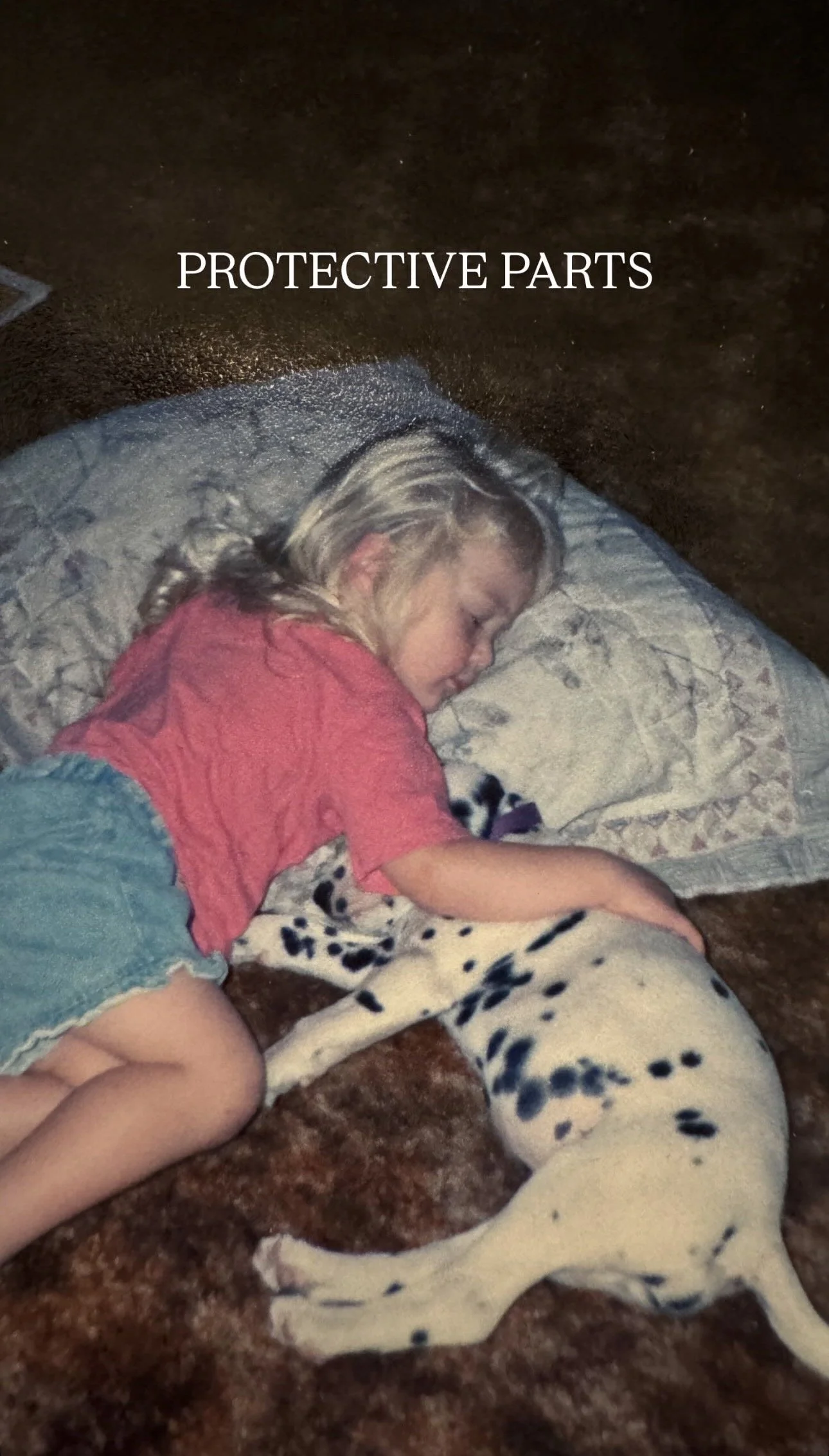 A young girl lying on a bed with a Dalmatian puppy, sleeping together. The girl has blonde hair and is wearing a pink shirt and jean shorts. The puppy is lying on its side with black spots.