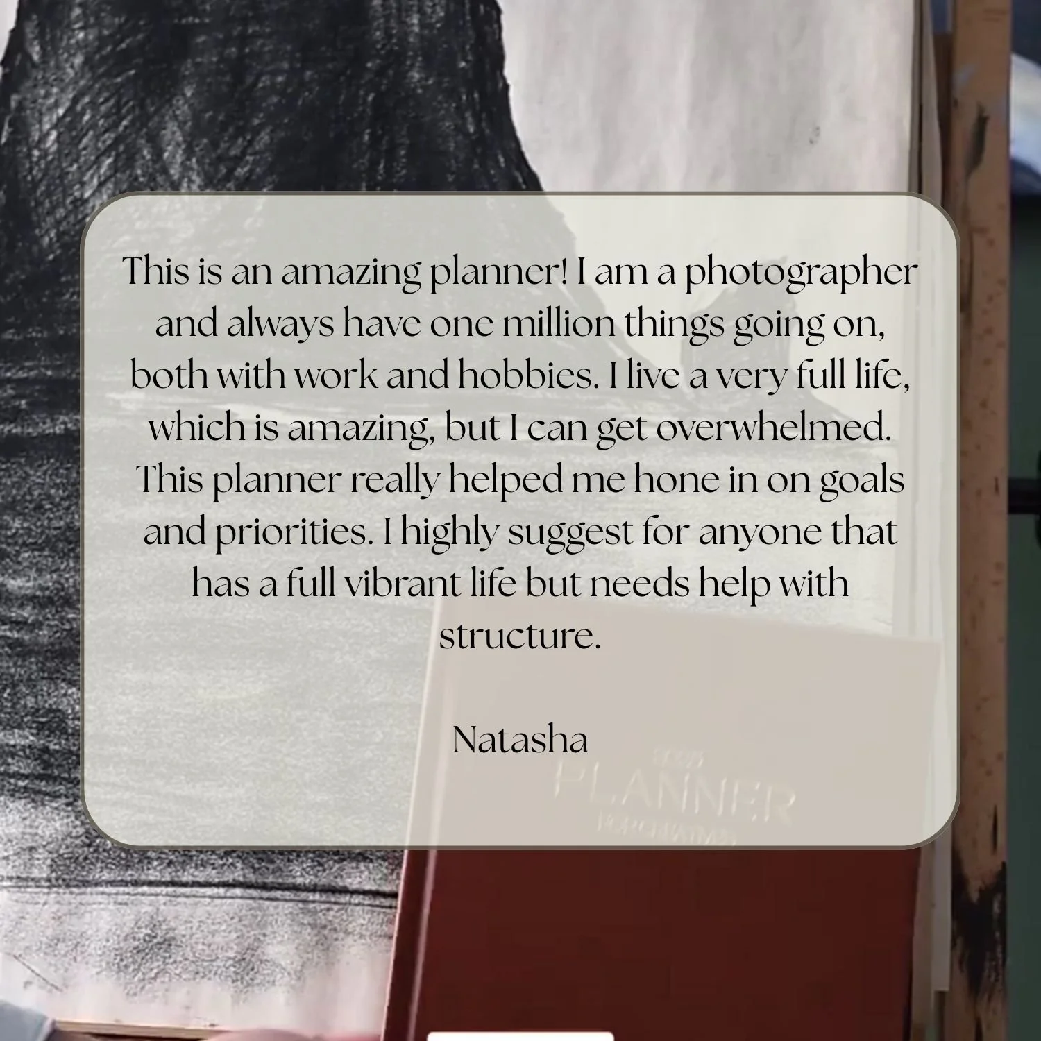 A close-up photo of a textured black and white artwork with a semi-transparent review overlay. The review discusses a planner, its usefulness, and recommends it for people with busy lives, signed by Natasha.