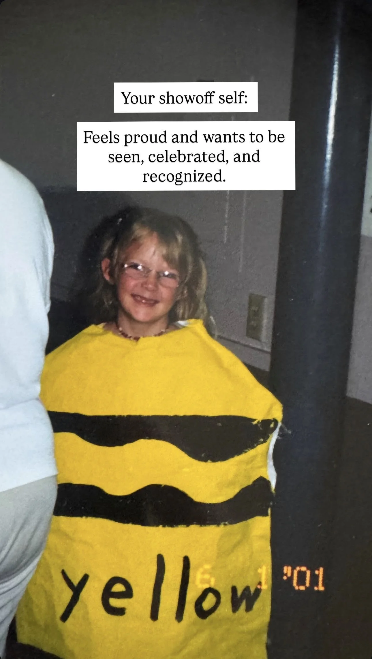 A young girl dressed in a yellow and black striped costume resembling a bumblebee, smiling at the camera in a dimly lit room.
