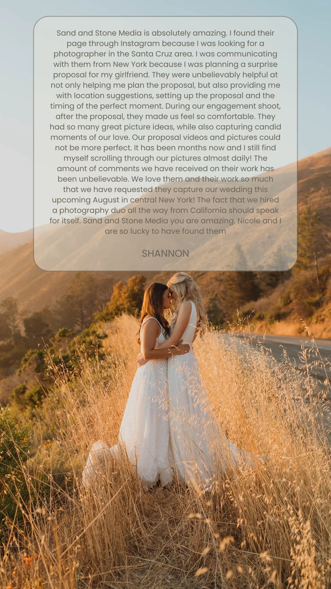 Two women in wedding dresses, embracing in a field of tall, golden grass during sunset with rolling hills in the background.