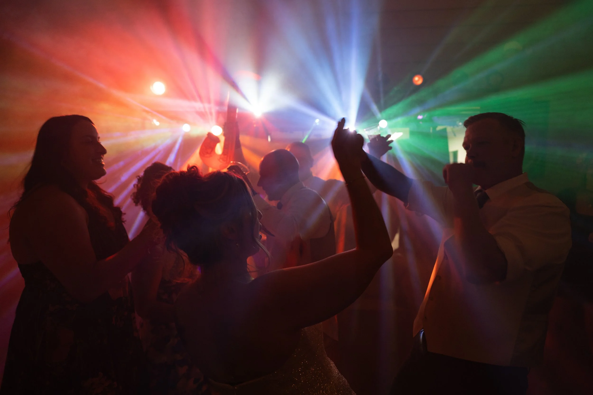 People dancing at a party with colorful lights and laser beams.