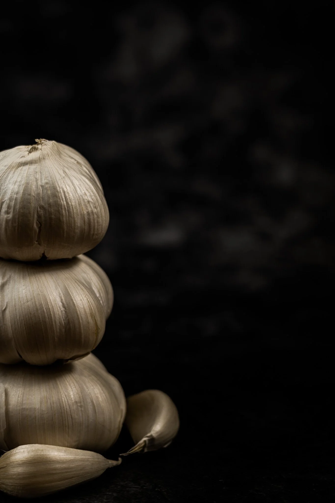A stack of three garlic bulbs with two garlic cloves on a dark surface.