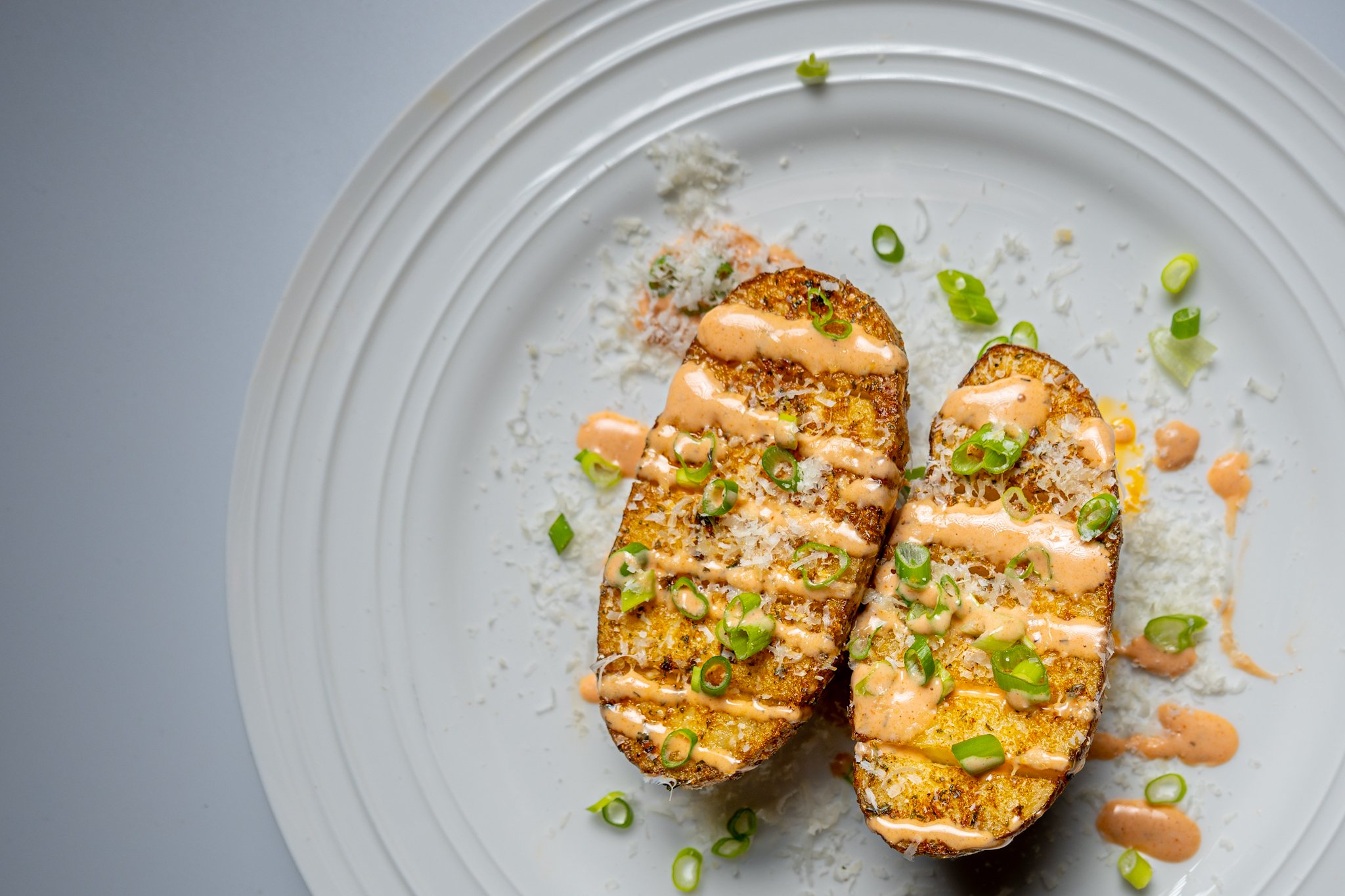 Two slices of grilled bread topped with a creamy sauce, green onions, and grated cheese on a white plate.