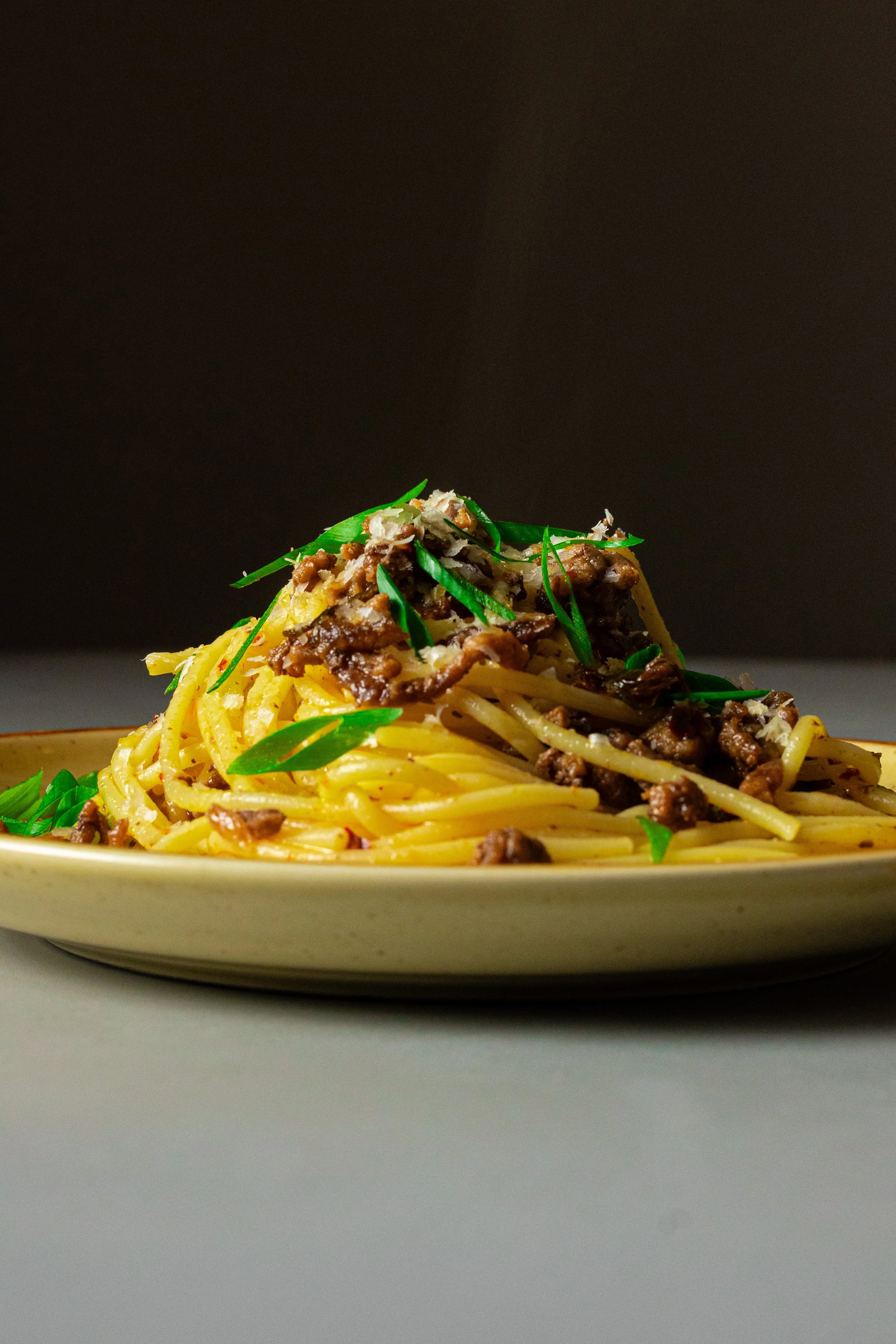 Plate of spaghetti with beef and green onion garnish on a neutral background.