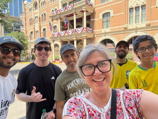 Group of six people smiling for a selfie on 6th Street in front of Driskill Hotel with American flags and patriotic bunting.