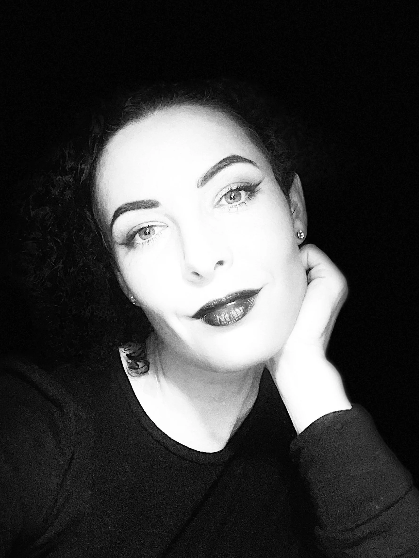 Black and white portrait of me wearing a dark top resting on my hand.