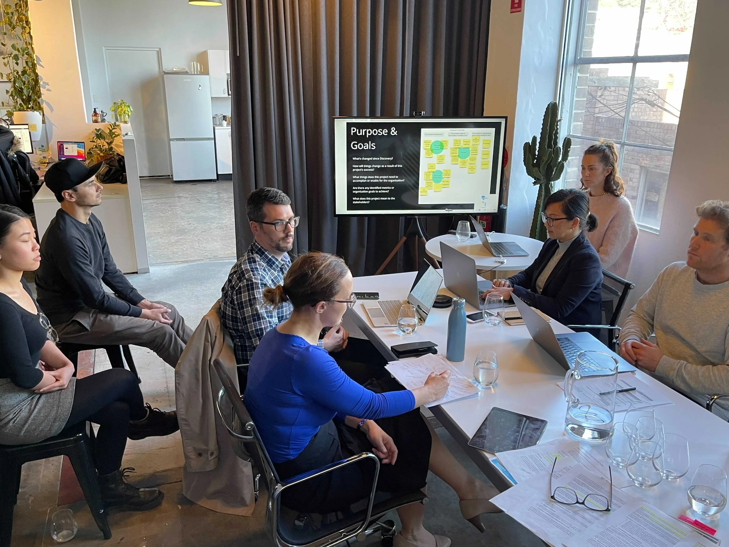 A group of people in a design studio sit around a table and discuss the context of the project in a workshop