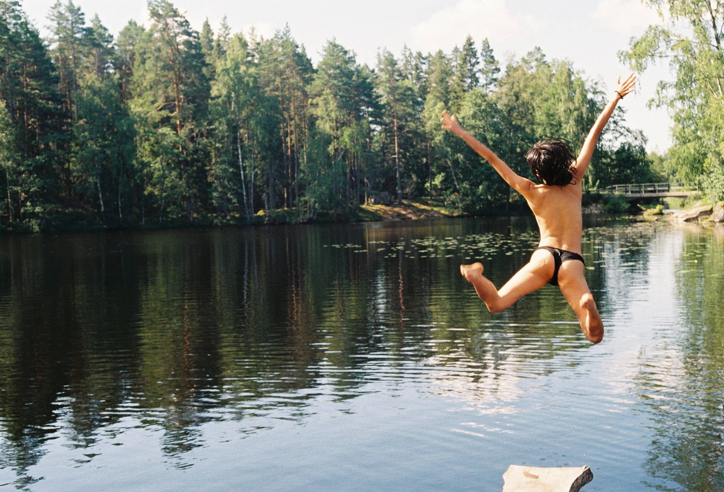 A person jumping into a lake at a retreat, surrounded by lush green trees on a sunny day.