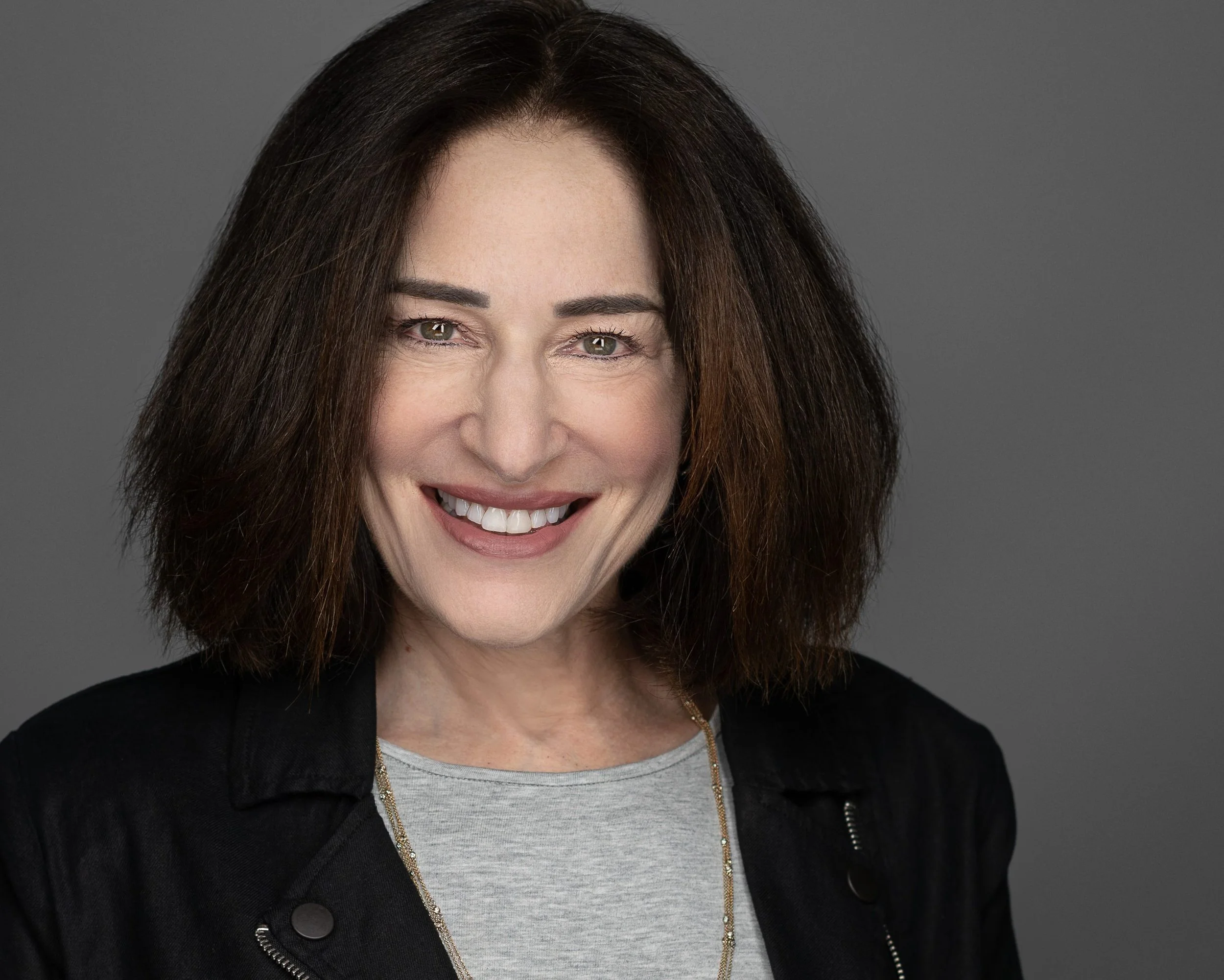 A woman with shoulder-length brown hair smiling against a gray background.