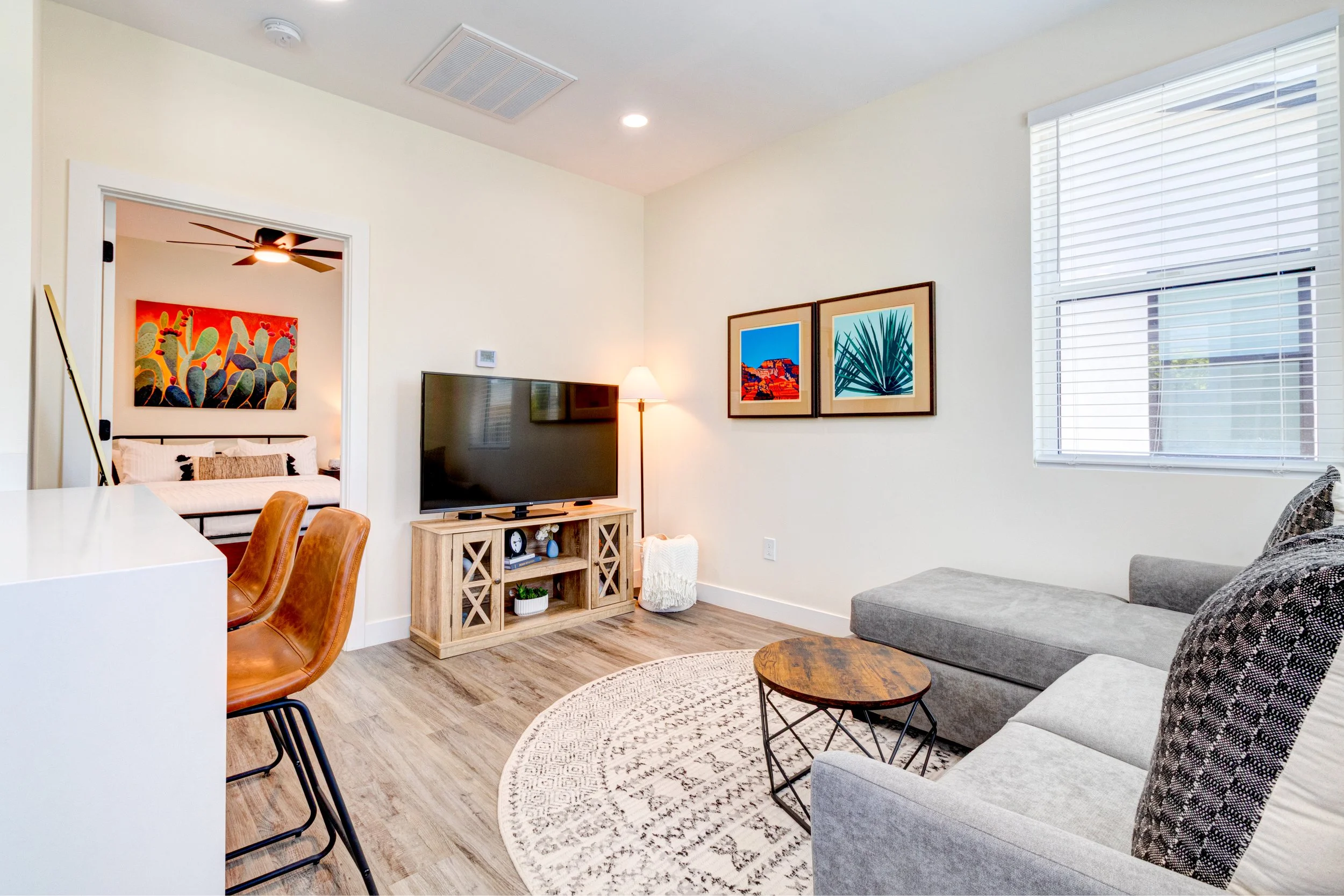 Small casita living room in Phoenix with a gray sectional sofa, wood TV console, breakfast bar, and an adjoining bedroom.