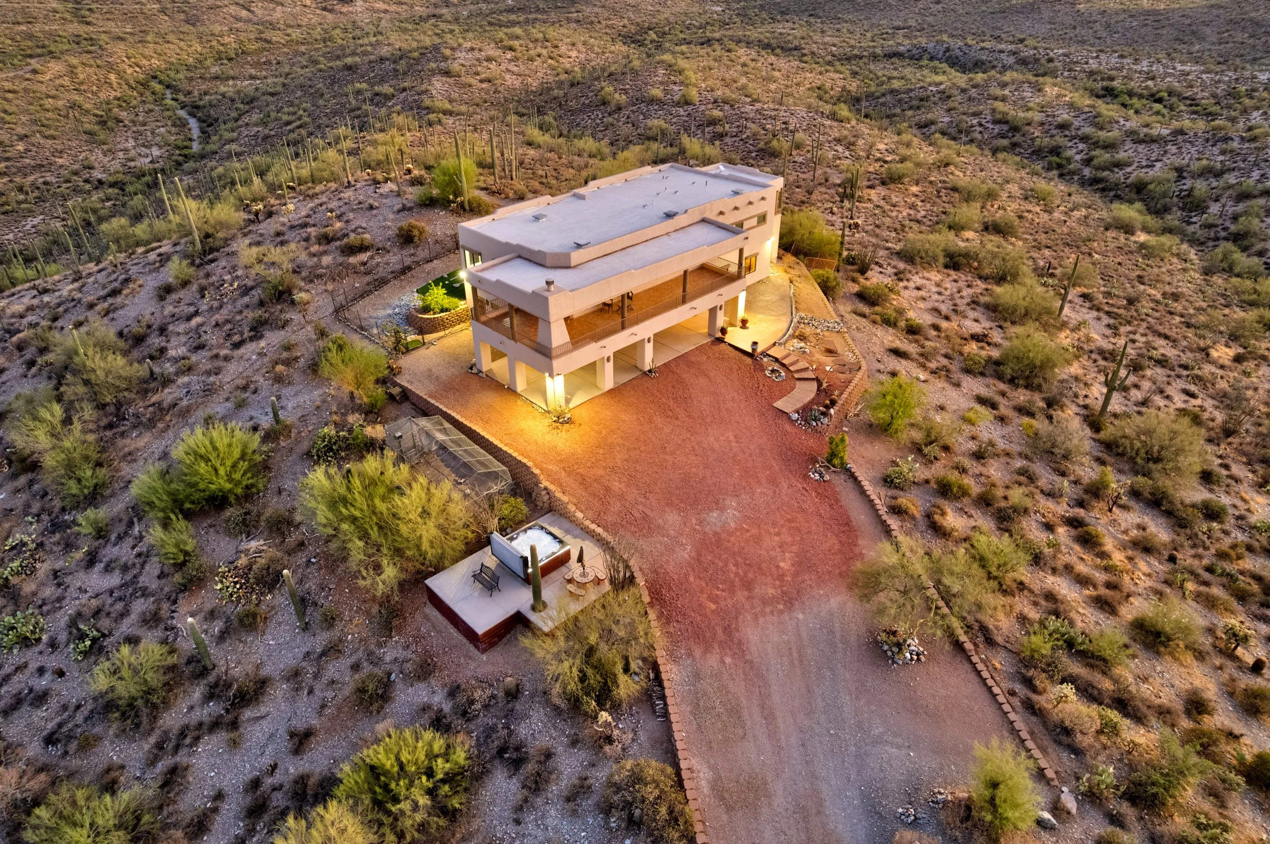 Aerial view of a desert home east of Mesa with a covered balcony, gravel driveway, and surrounding saguaro cacti.