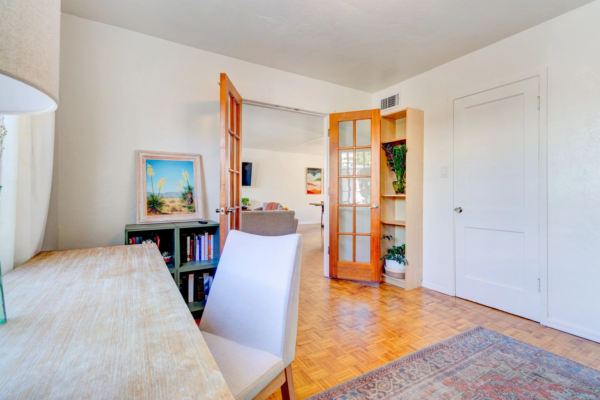Home office in Phoenix’s Arcadia area with a desk, upholstered chair, wood flooring, and glass-paneled doors.