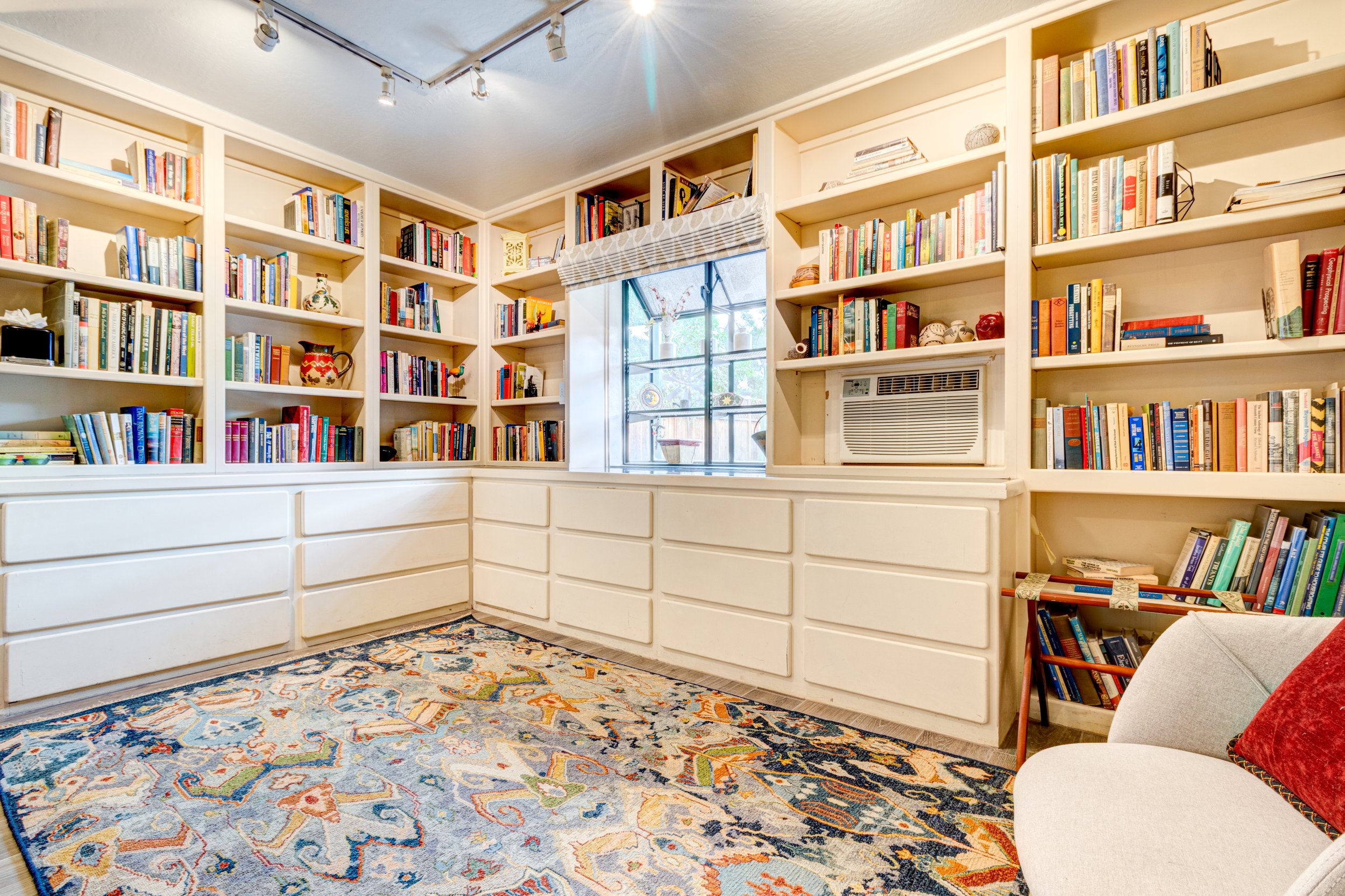 Home library nook with built-in bookshelves, white storage drawers, and a patterned rug.