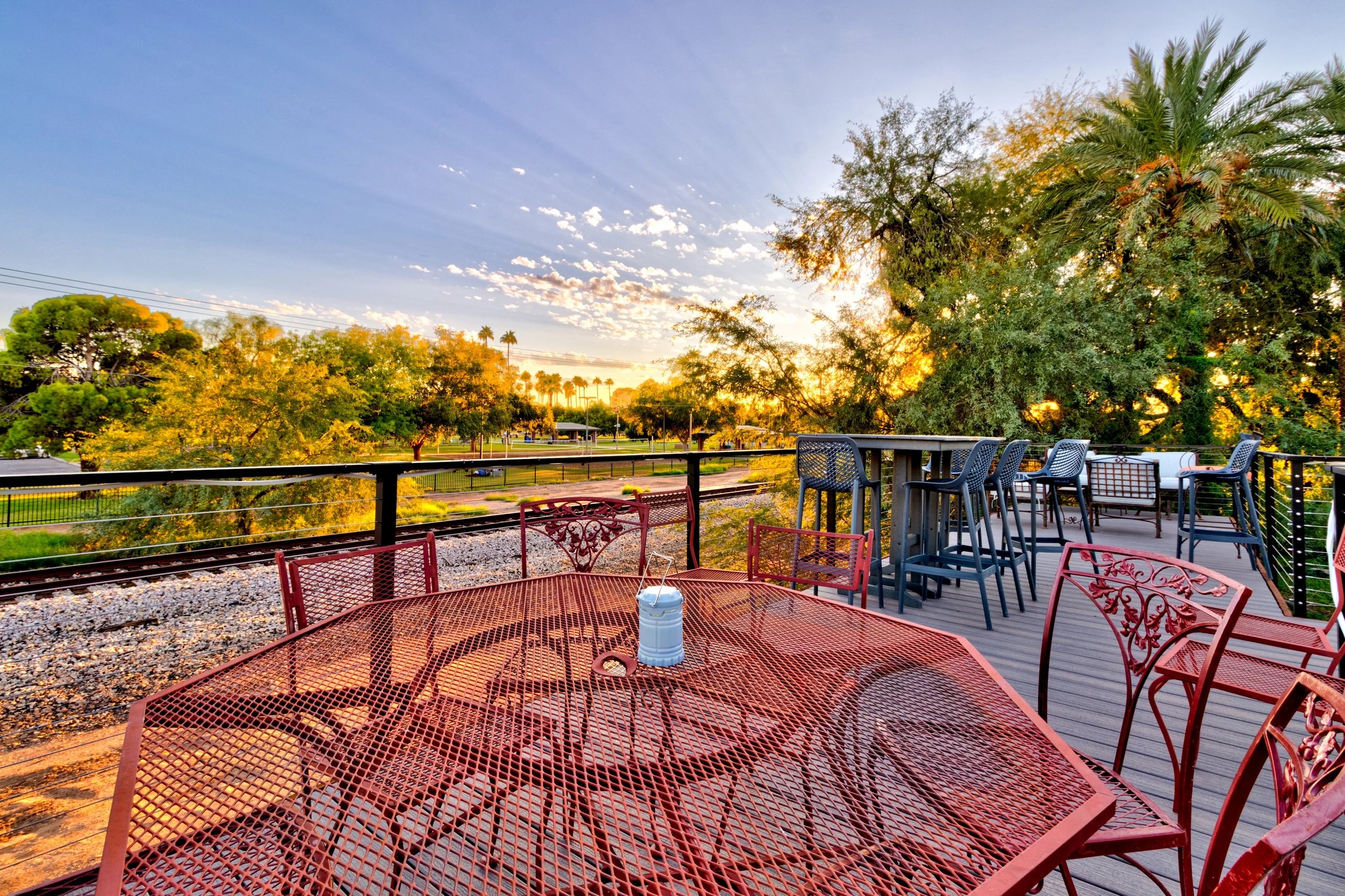 Tempe backyard patio with circular brick paving and a metal railing overlooking a park and railway tracks at sunset.