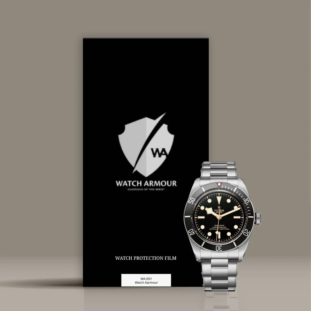 A black Watch Armour protection film package with a shield logo, a wristwatch with a black dial, silver bezel, and metal bracelet placed in front of it.