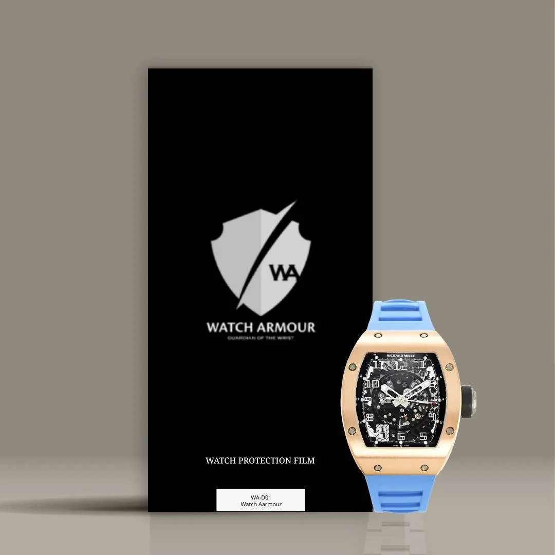 A luxury watch with a black face and multiple dials, attached to a blue strap, resting against a black box with a watch protection film label.