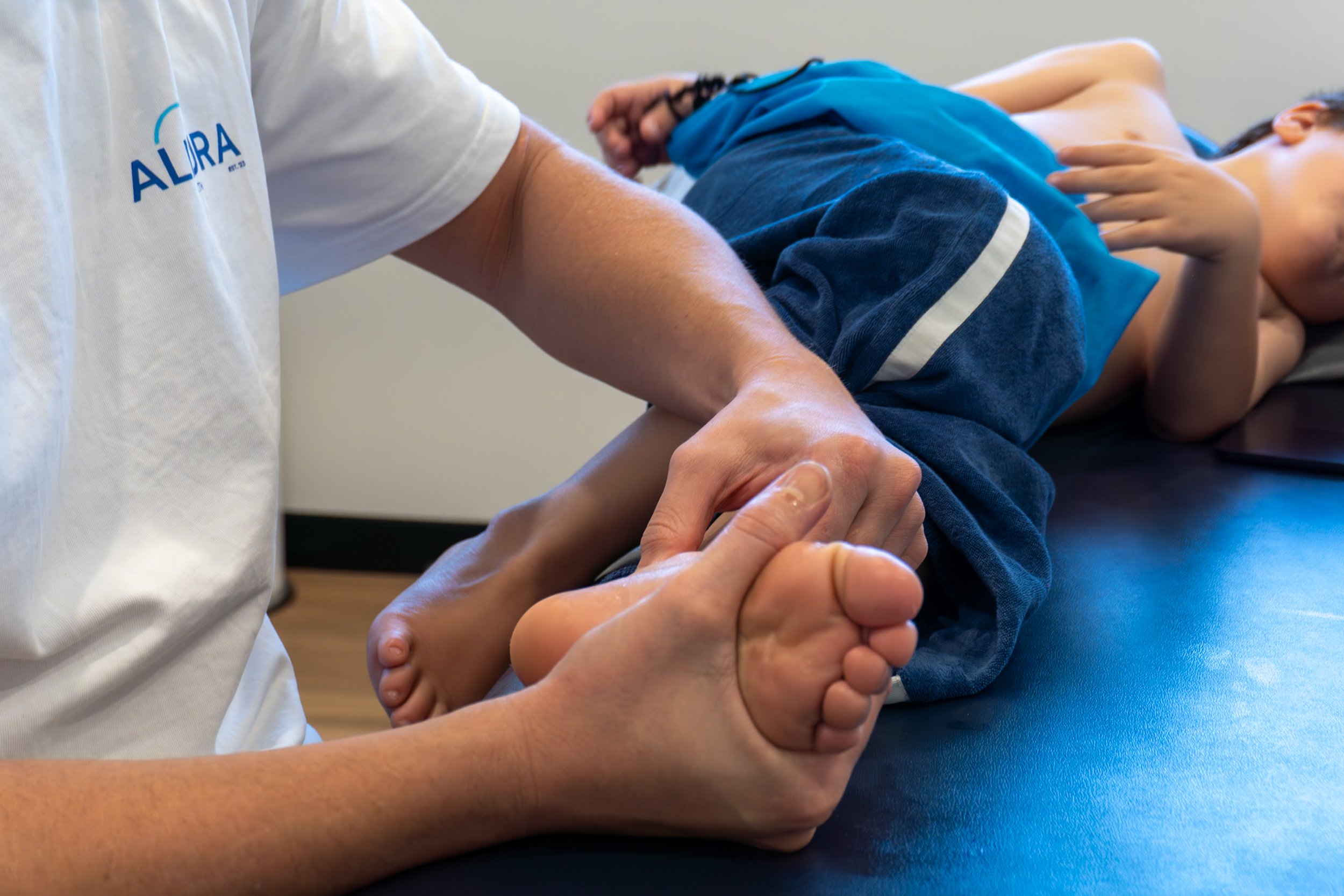 Child lying on examination table receiving physical therapy for foot and ankle. Physical therapist holding child's foot.
