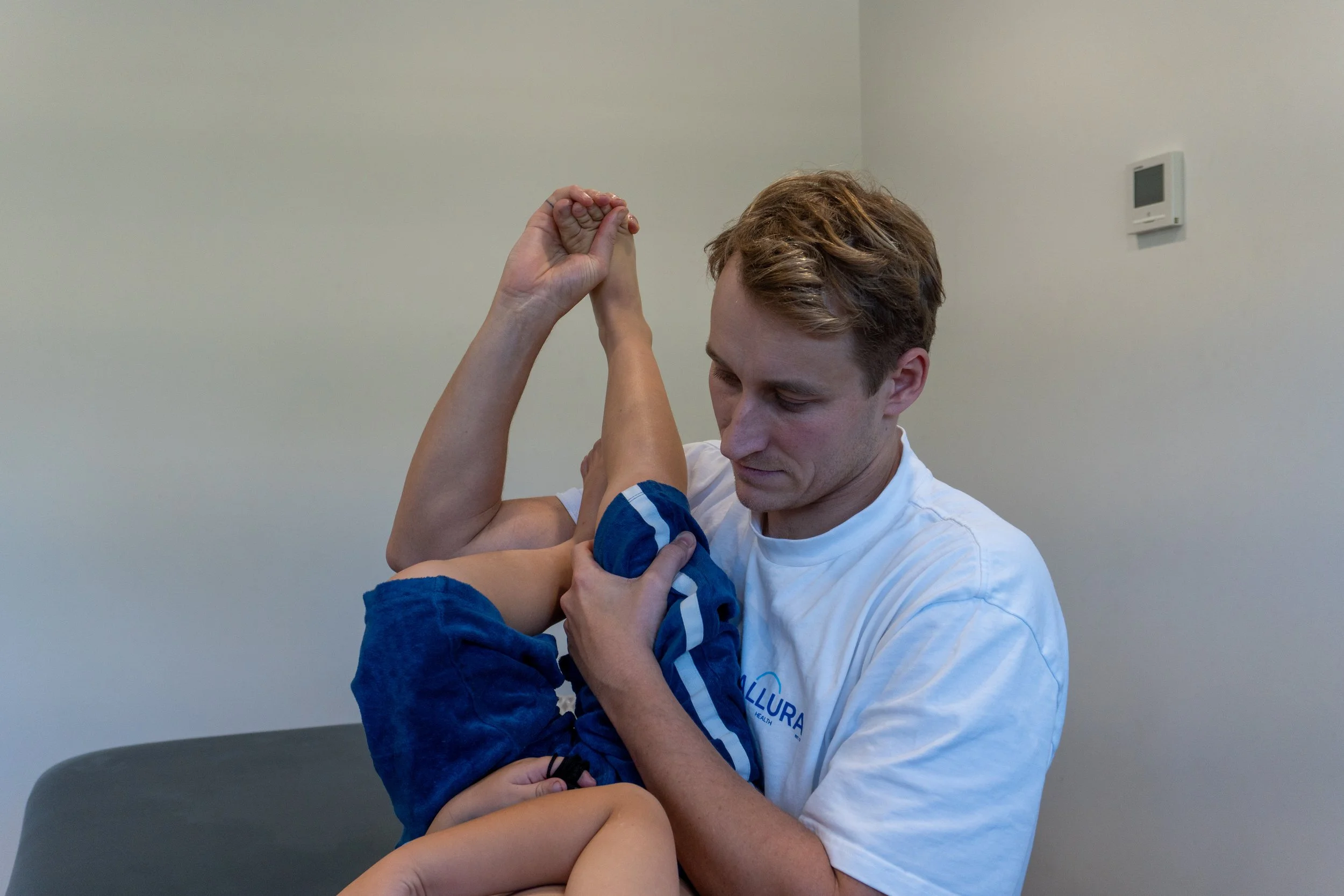 A physical therapist practicing arm stretching exercises with a young boy in a clinical setting.