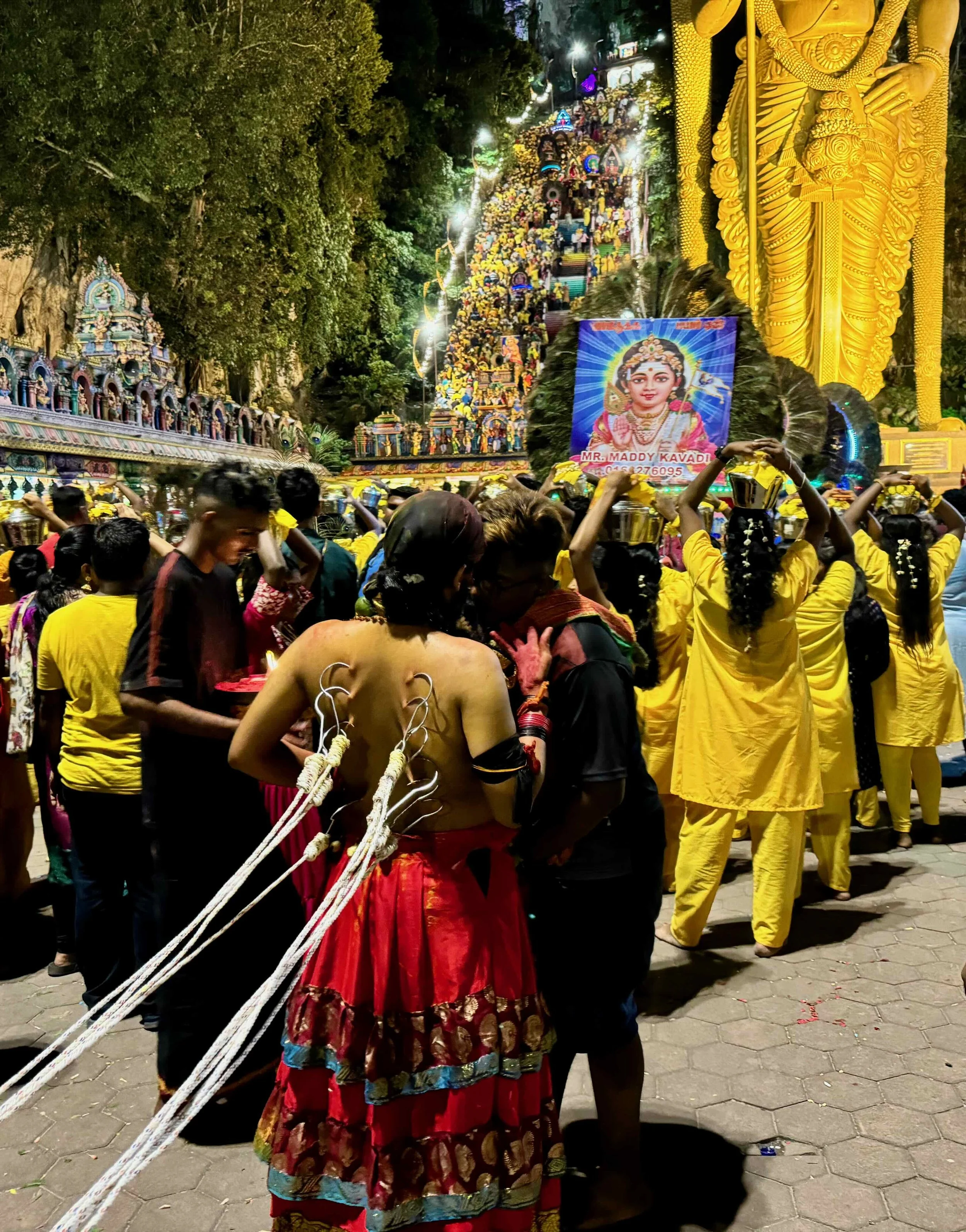 A Thaipusam pilgrim with hooks piercing his back attached to ropes held by companions.